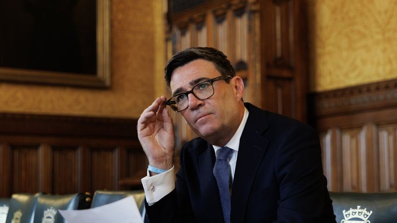 Andy Burnham seated at a table in his Parliamentary Office, adjusting his glasses, with papers in front of him.