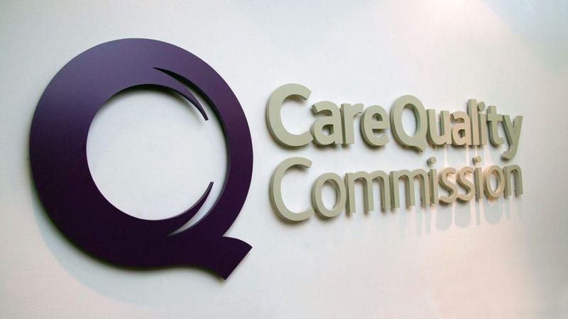 The Care Quality Commission’s sign on a white wall: a large purple Q beside the words Care Quality Commission.