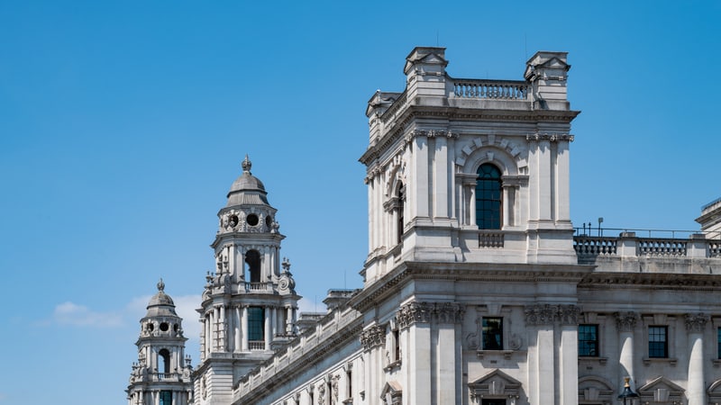Ornate white stone towers and upper floors of the HM Treasury building against a clear blue sky