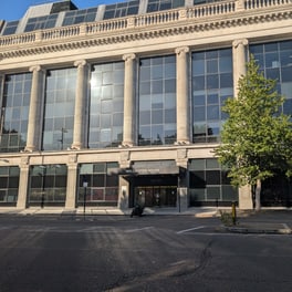 Stone and glass office building with tall columns and a sign reading Wellington House above the entrance, a young tree on the pavement and an empty road in front