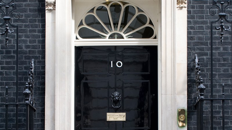 The black front door of 10 Downing Street, with its white number 10, a lion's-head knocker and a fanlight above.
